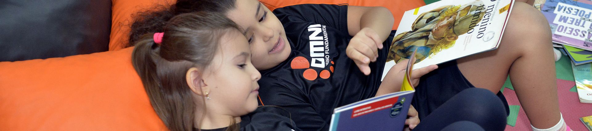 Duas alunas das Séries Iniciais do OMNI lendo juntas na biblioteca